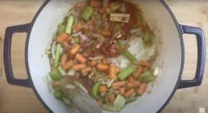 Vegetable stew prep: onions, carrots, celery, and tomato in a pot, ready for cooking on a wooden board.